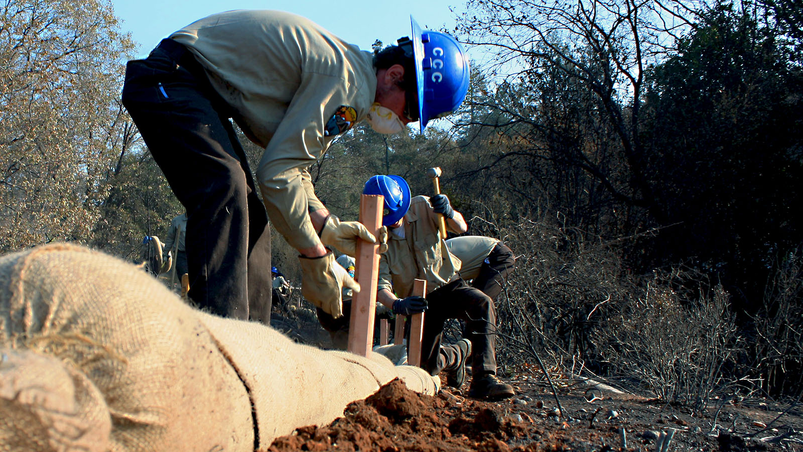 Corpsmembers with the Placer 1 fire crew cut fire line with hand tools as flames from the Dixie Fire approach in 2021.