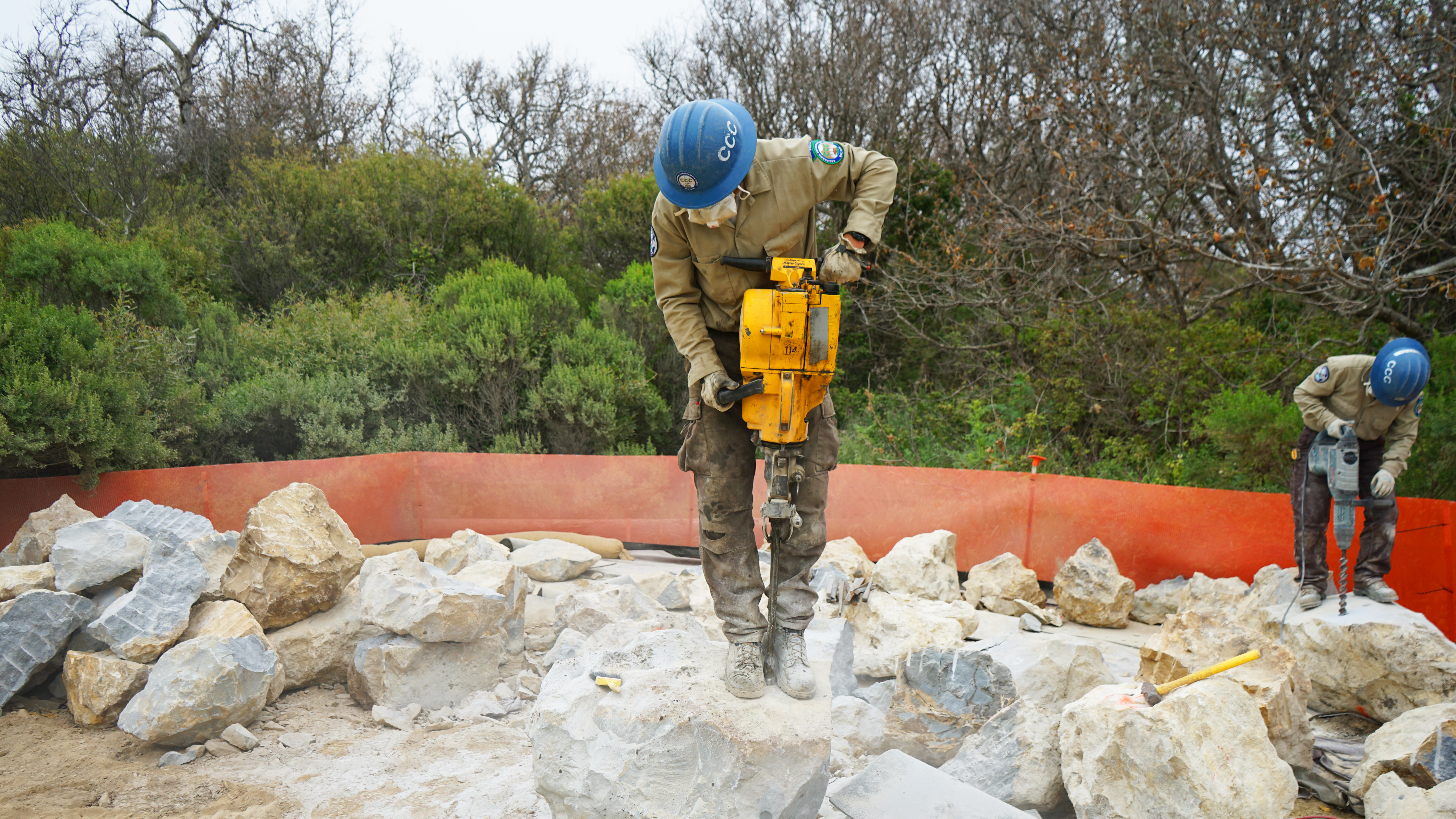 Two Corpsmembers drill holes into rock.