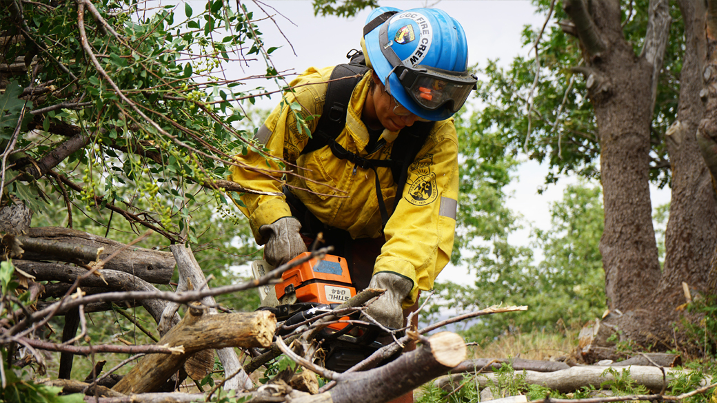 female firefighter using chain saw to cut up tree limbs