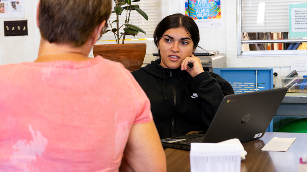 female sitting at laptop talking to teacher