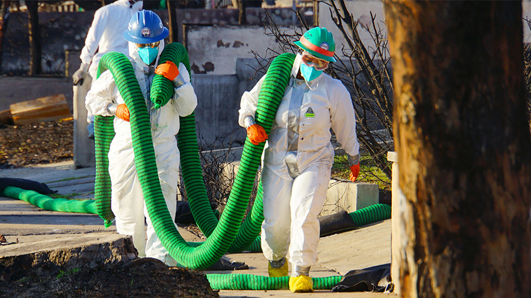 corpsmembers in protective suits hauling silt sock down a street