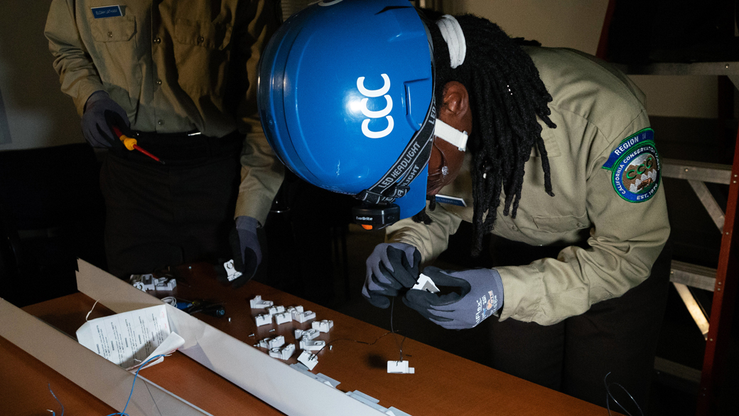 male in helmet and eye pro bending over table using his hands to build a light tombstone device