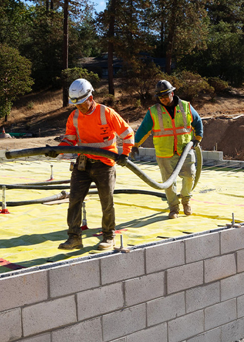 Greenwood_Construction_ConstruxWorkers_500x700 two construction workers holding cement pump hose