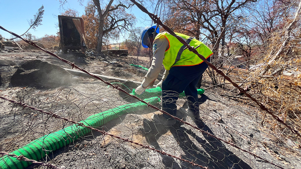 corpsmember in safety vest lays out a green silt sock, with barbed wire in the foreground