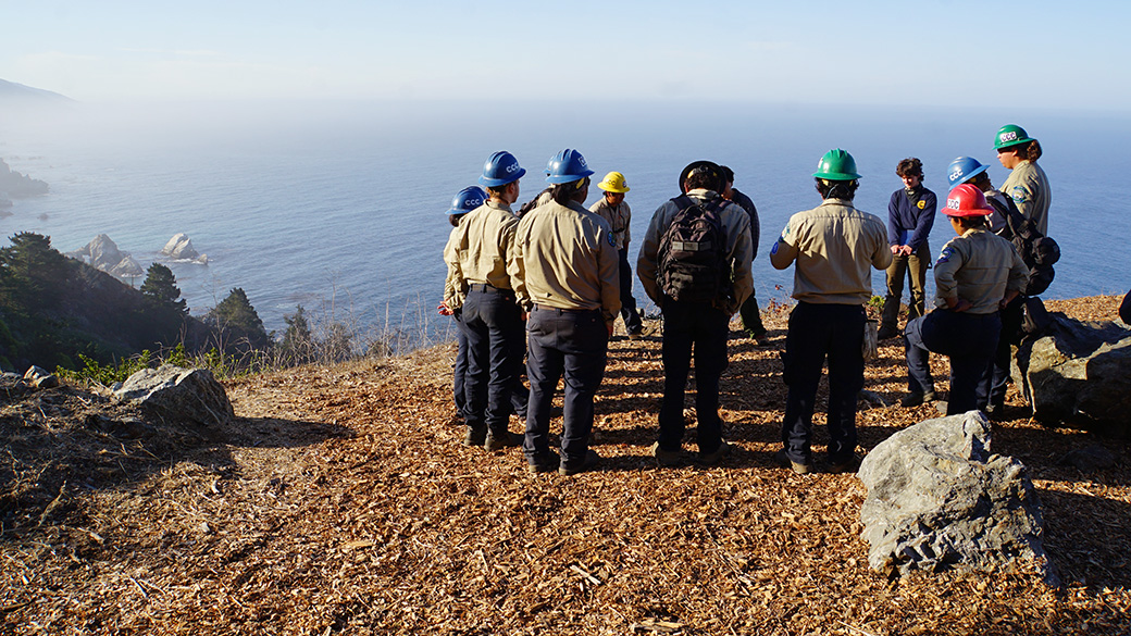 corpsmembers and state parks standing in circle atop bluff overlooking pacific ocean
